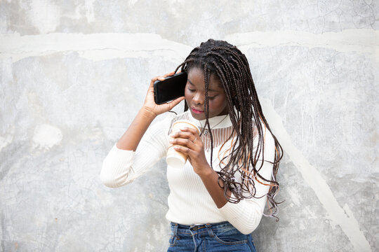 Portrait Of Beautiful Young African American Woman Showing Long Black Hair Braided Hairstyle And Using Mobile Phone While Feeling Happy And Smiling In The City Outdoor