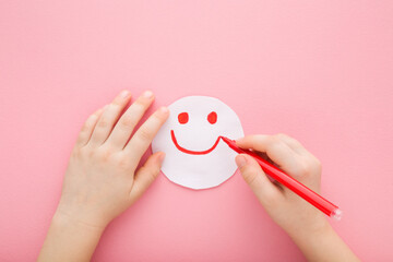Baby girl hand holding red marker and drawing smiley. Happy smiling face expression on white paper....