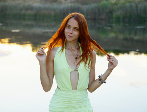 Selfie portraits of a red-haired woman in a yellow fantasy cocktail dress on the beach next to the water on a hot summer evening/ 