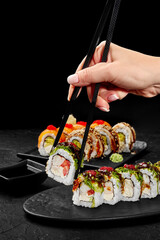 Female hand taking shrimp sushi roll from plate with chopsticks