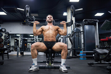 Fototapeta na wymiar Muscular man with dark hair doing exercise with training apparatus in gym. Low angle view of strong male athlete sitting, using sport equipment during workout. Sport, weight lifting concept.