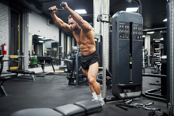 Middle-aged Caucasian man training in crossover machine indoors. Side view of bearded crossfit male...