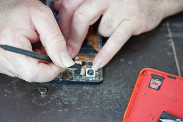 hands of a technician disassembling a mobile phone, with the help of some hand tools, such as...