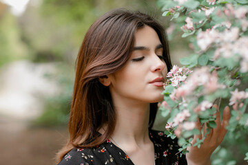 Side view of pretty, young female admiring blooming tree, looking down, holding branch, smelling...