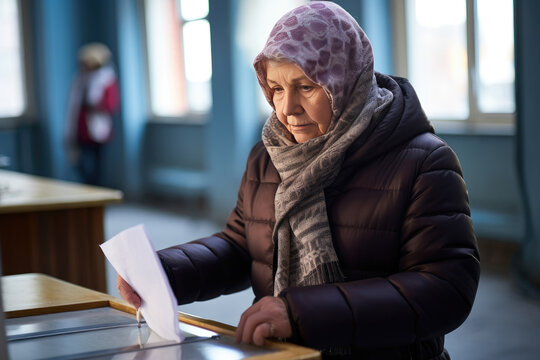 Senior woman in warm clothes putting a ballot into a voting box during elections