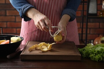 Woman peeling fresh potato at wooden table indoors, closeup