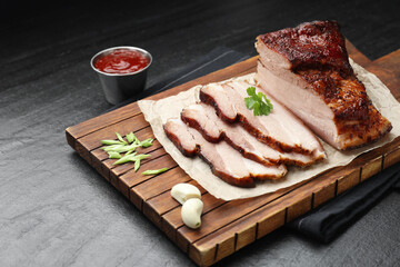Pieces of baked pork belly served with sauce and parsley on black textured table