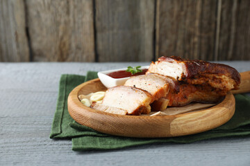 Pieces of baked pork belly served with sauce on grey wooden table, space for text