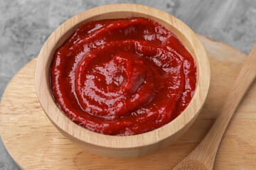 Organic ketchup in wooden bowl and spoon on grey table, closeup. Tomato sauce