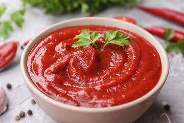 Organic ketchup and parsley in bowl on grey table, closeup. Tomato sauce