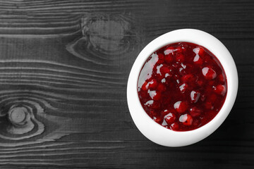 Fresh cranberry sauce in bowl on black wooden table, top view. Space for text