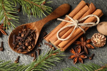 Wooden spoon with different spices, nuts and fir branches on gray table, flat lay