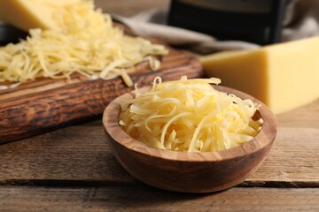 Grated cheese in bowl on wooden table, closeup