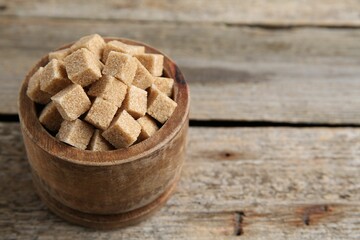 Bowl with brown sugar cubes on wooden table, closeup. Space for text