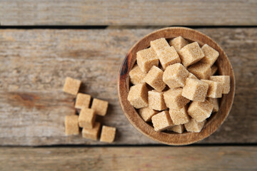 Bowl with brown sugar cubes on wooden table, top view