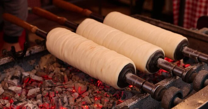 4k movie of delicious Kurtoskalacs, known locally as colac secuiesc, a spit cake traditional from Ardeal,Transylvania baking on hot charcoal at a typical open air market street bakers.