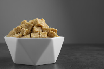 Brown sugar cubes in bowl on grey table. Space for text