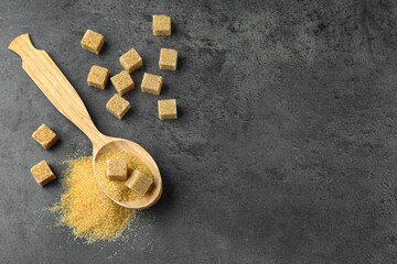 Spoon with brown sugar cubes on grey table, flat lay. Space for text