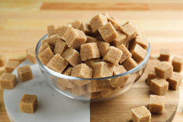 Brown sugar cubes in bowl on wooden table, closeup