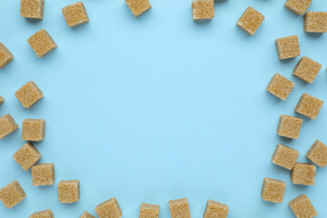 Frame of brown sugar cubes on light blue background, flat lay. Space for text