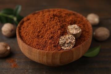 Nutmeg powder and halves of seed in bowl on wooden table, closeup