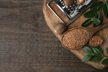 Spoon with grated nutmeg, seeds, grater and green branches on wooden table, top view. Space for text
