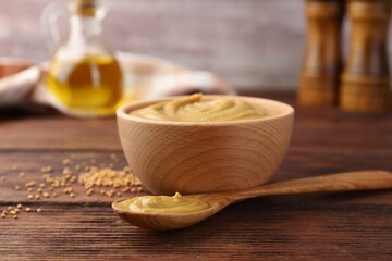 Bowl and spoon with tasty mustard sauce on wooden table, closeup