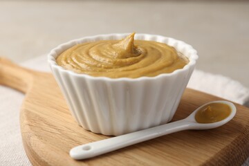 Bowl and spoon with tasty mustard sauce on light table