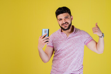 Front view of brunette, handsome male with beard posing indoors, smiling, holding smartphone, taking photo. Concept of youth.