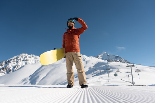 snowboarder holding snowboard standing and posing along ski slope at  resort prepared by snowcat