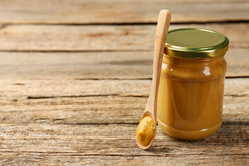 Jar and spoon with tasty mustard sauce on wooden table, space for text