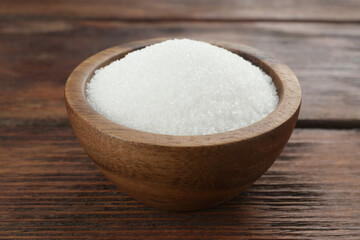 Fototapeta na wymiar Granulated sugar in bowl on wooden table, closeup