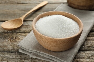 Granulated sugar in bowl and spoon on wooden table, closeup