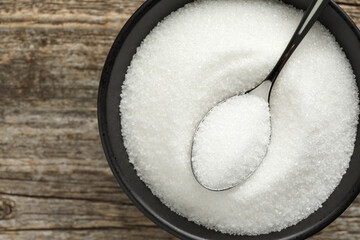 Granulated sugar in bowl and spoon on wooden table, top view. Space for text