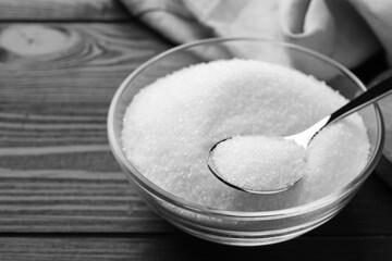 Granulated sugar in bowl and spoon on black wooden table, closeup. Space for text