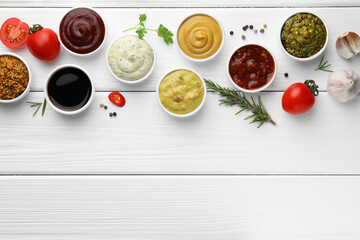 Many different sauces, spices and vegetables on white wooden table, flat lay. Space for text