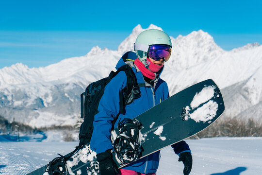 Snowboarder woman standing with snowboard in beautiful mountain peaks covered with snow on background