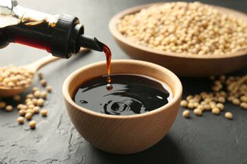Pouring tasty soy sauce from bottle into bowl on black table, closeup