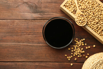 Soy sauce in bowl and soybeans on wooden table, flat lay. Space for text