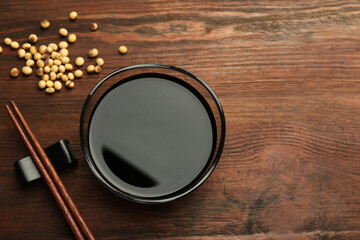 Soy sauce in bowl, soybeans and chopsticks on wooden table, flat lay. Space for text