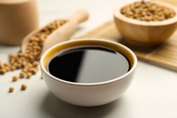 Soy sauce in bowl and soybeans on white table