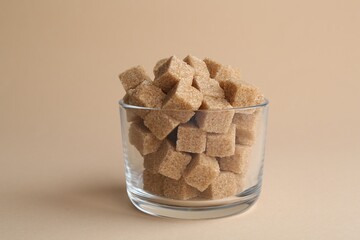 Brown sugar cubes in glass on beige background, closeup