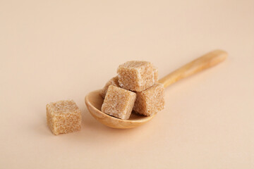 Brown sugar cubes and spoon on beige background, closeup