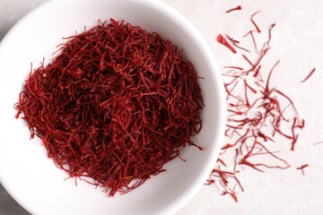 Aromatic saffron in bowl on light table, top view