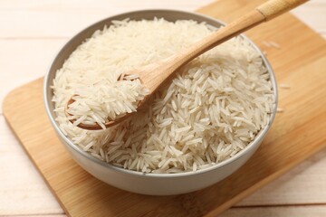 Raw basmati rice and spoon in bowl on wooden table