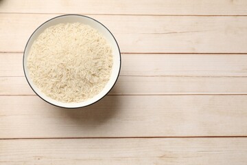 Raw basmati rice in bowl on white wooden table, top view. Space for text