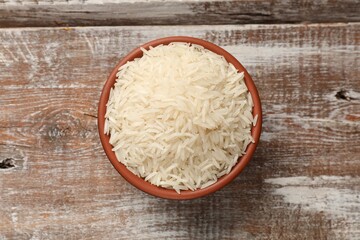 Raw basmati rice in bowl on wooden table, top view