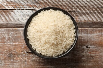 Raw basmati rice in bowl on wooden table, top view
