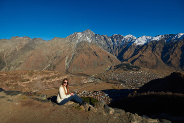 A beautiful lady posing in front of majestic brown mountains, their snowy tops shining in the...