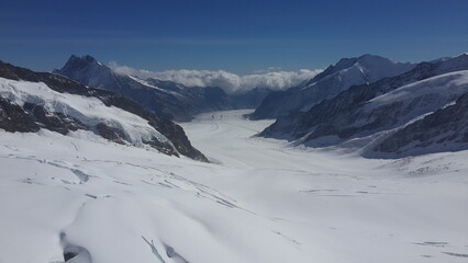 스위스 인터라켄의 융프라우 전망대에서 바라본 만년설에 휩싸인 설산의 풍경과 그 산 봉우리에 걸쳐진 풍성한 구름, 그리고 융프라우에서 개장한 눈썰매장을 위에서 내려다 본 장면, 설산의 봉우리에 걸친 높고 푸른 하늘과 하얀 뭉게구름 풍경입니다.  